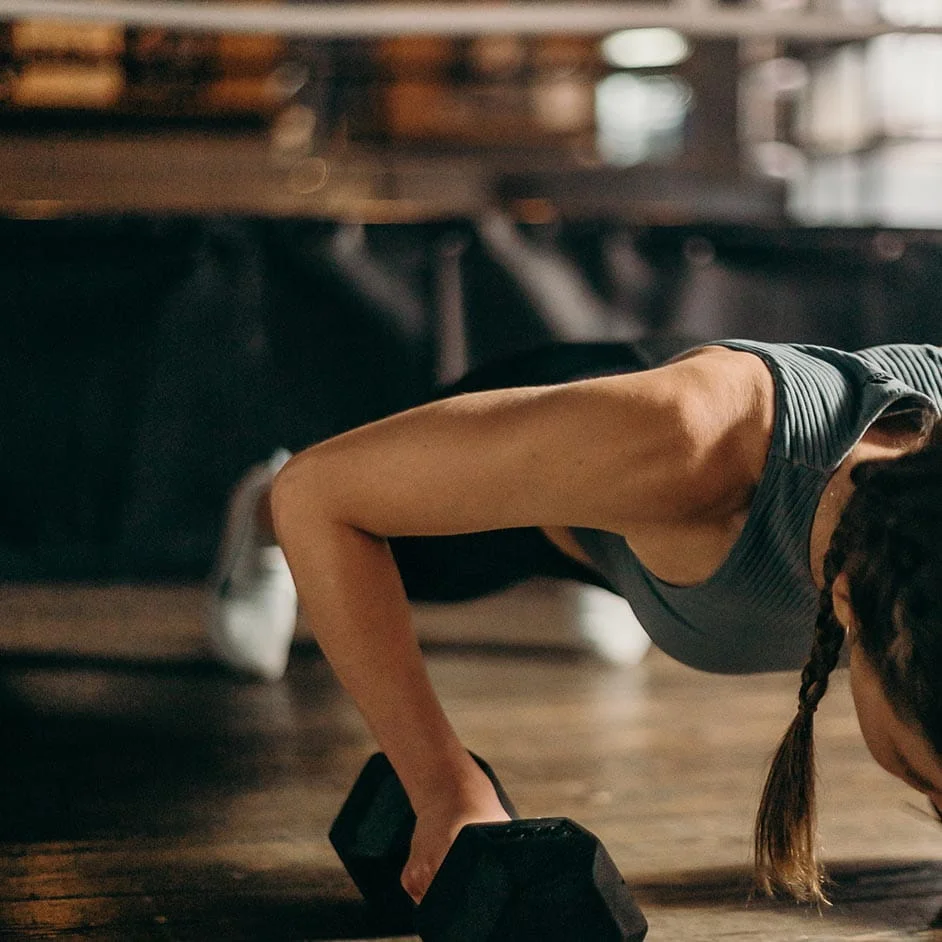 Persona realizando un ejercicio de fuerza con mancuernas en un gimnasio